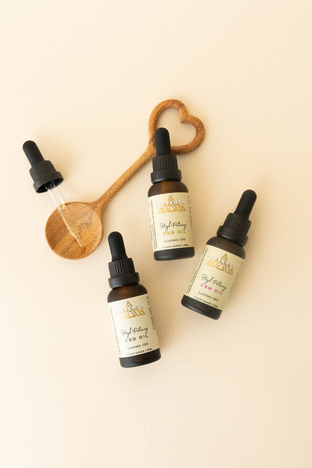 Three amber glass dropper bottles of GriefDay CBD Oil with cream labels, arranged on a light beige background with a wooden spoon and a glass dropper.