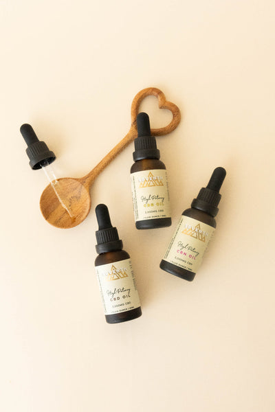Three amber glass dropper bottles of GriefDay CBD Oil with cream labels, arranged on a light beige background with a wooden spoon and a glass dropper.