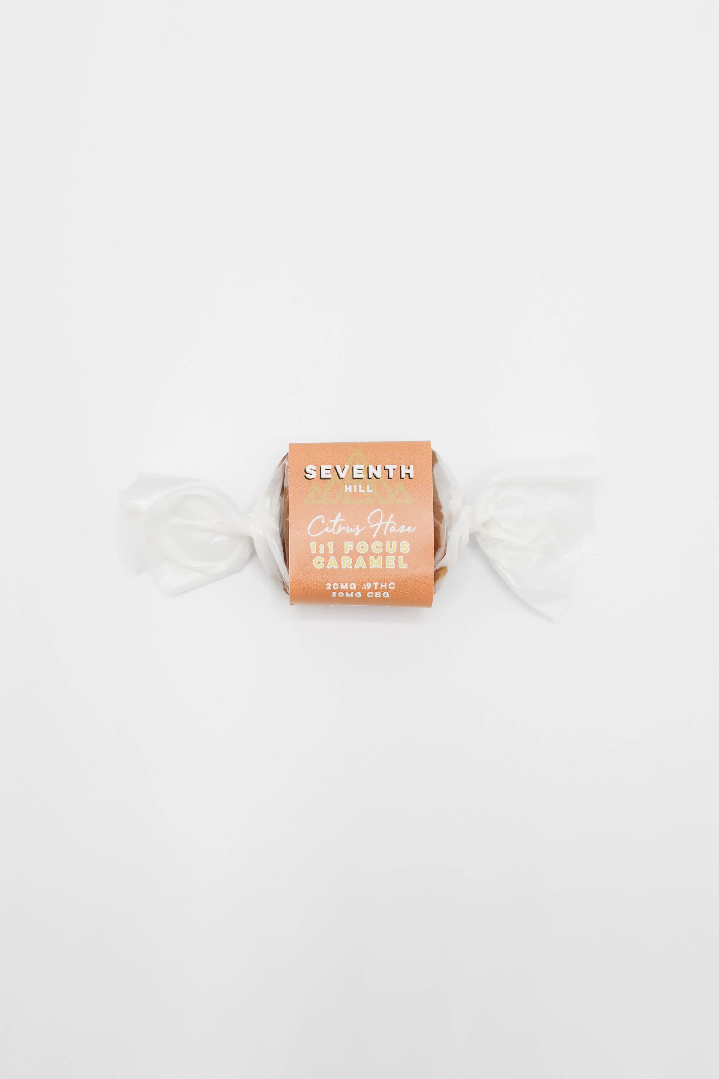 A single wrapped piece of caramel on a plain white background. The wrapper is a warm peach-orange color with white text reading 'SEVENTH HILL' and 'Citrus Haze CBG Focus Caramel', and the candy is wrapped in wax paper with white wrapper tails on each side.