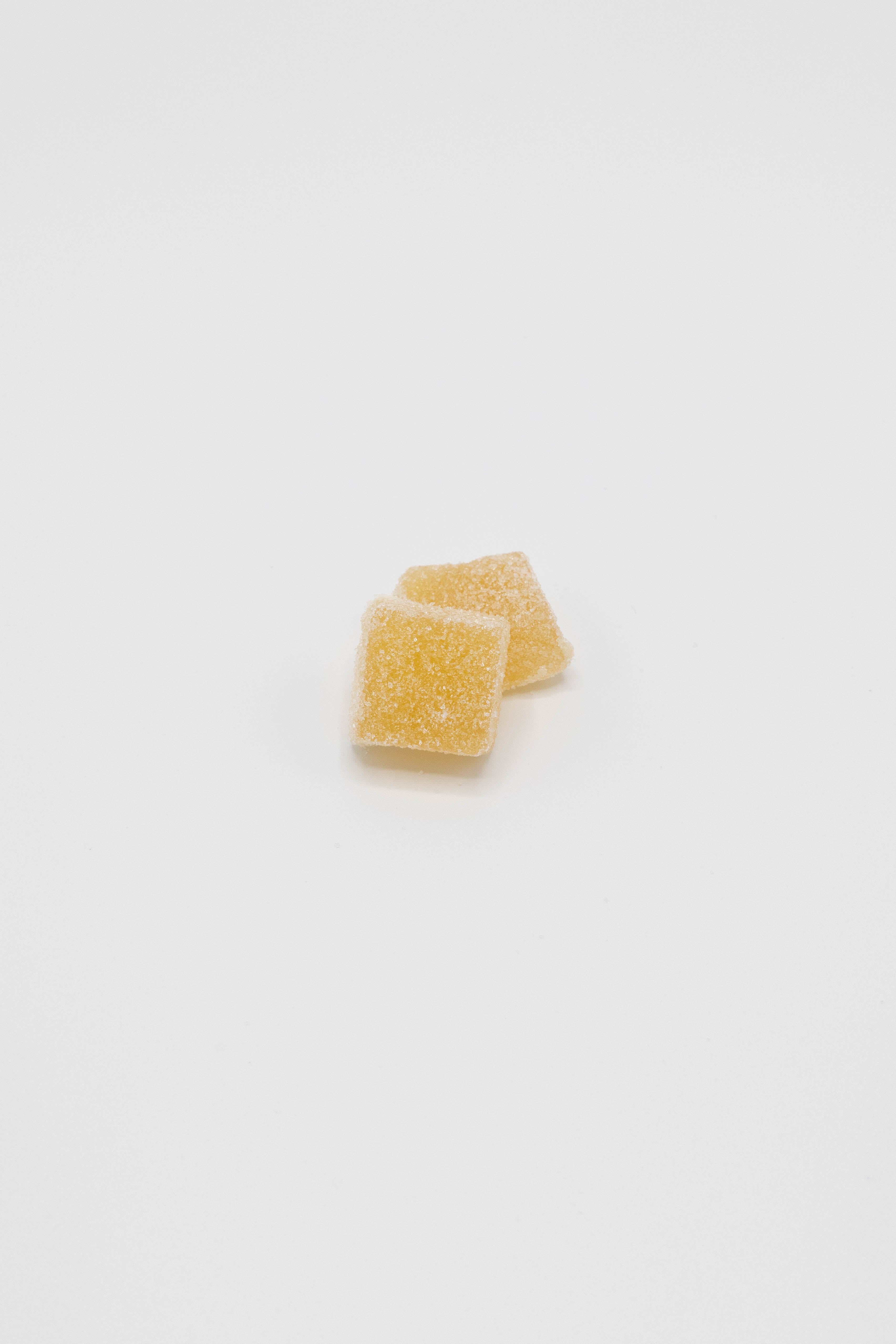 Two small, square, translucent yellow gummy candies with a sugar coating, stacked on a plain white background.