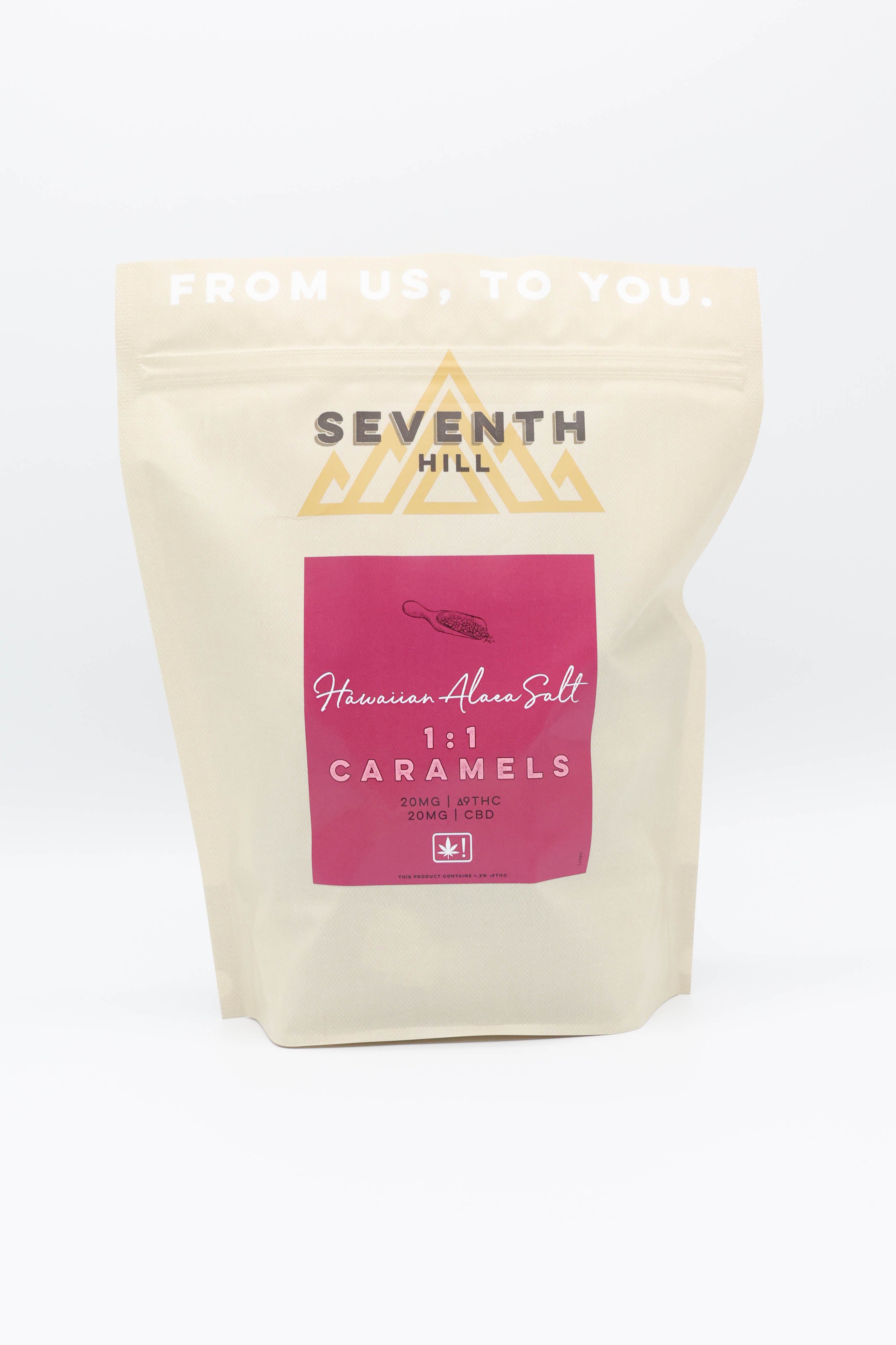 A stand-up pouch of Seventh Hill Hawaiian Alaea Salt 1:1 Caramels on a clean white background. The pouch is a warm cream color with a prominent magenta label and gold logo.
