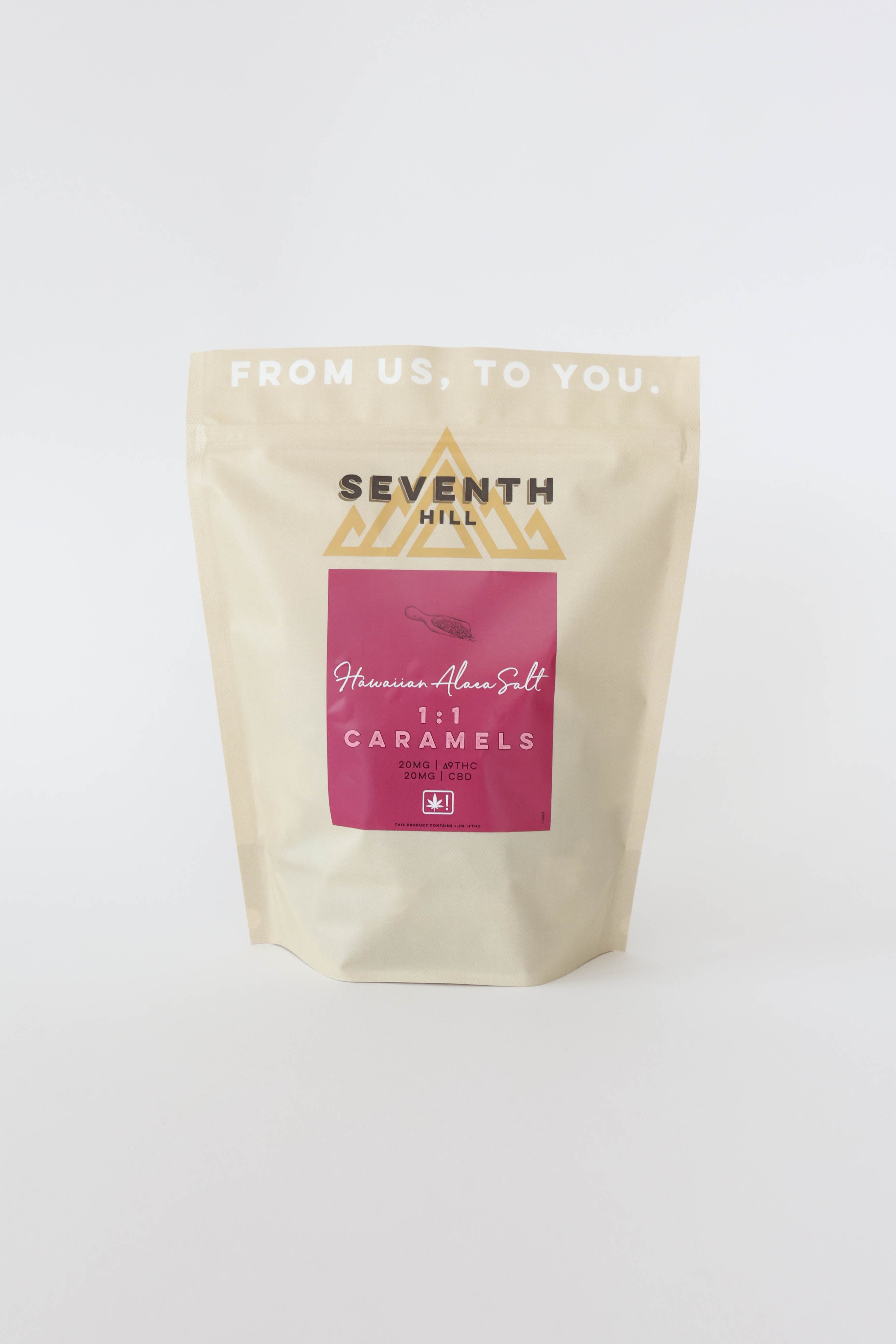 A stand-up pouch of Seventh Hill 1:1 Hawaiian Alaea Salt Caramels on a clean white background. The packaging is a light cream color with a prominent magenta-pink label in the center and gold logo details.
