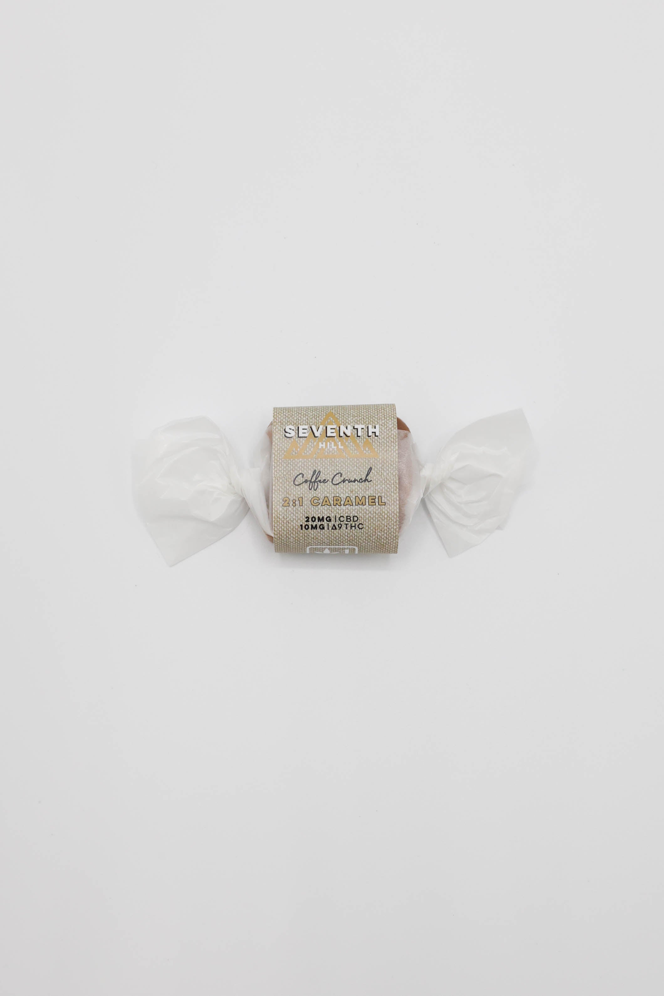 A single wrapped piece of caramel from Seventh Hill, specifically '2:1 Coffee Crunch' , wrapped in cream paper and a wax paper sleeve with gold lettering, set against a plain white background.