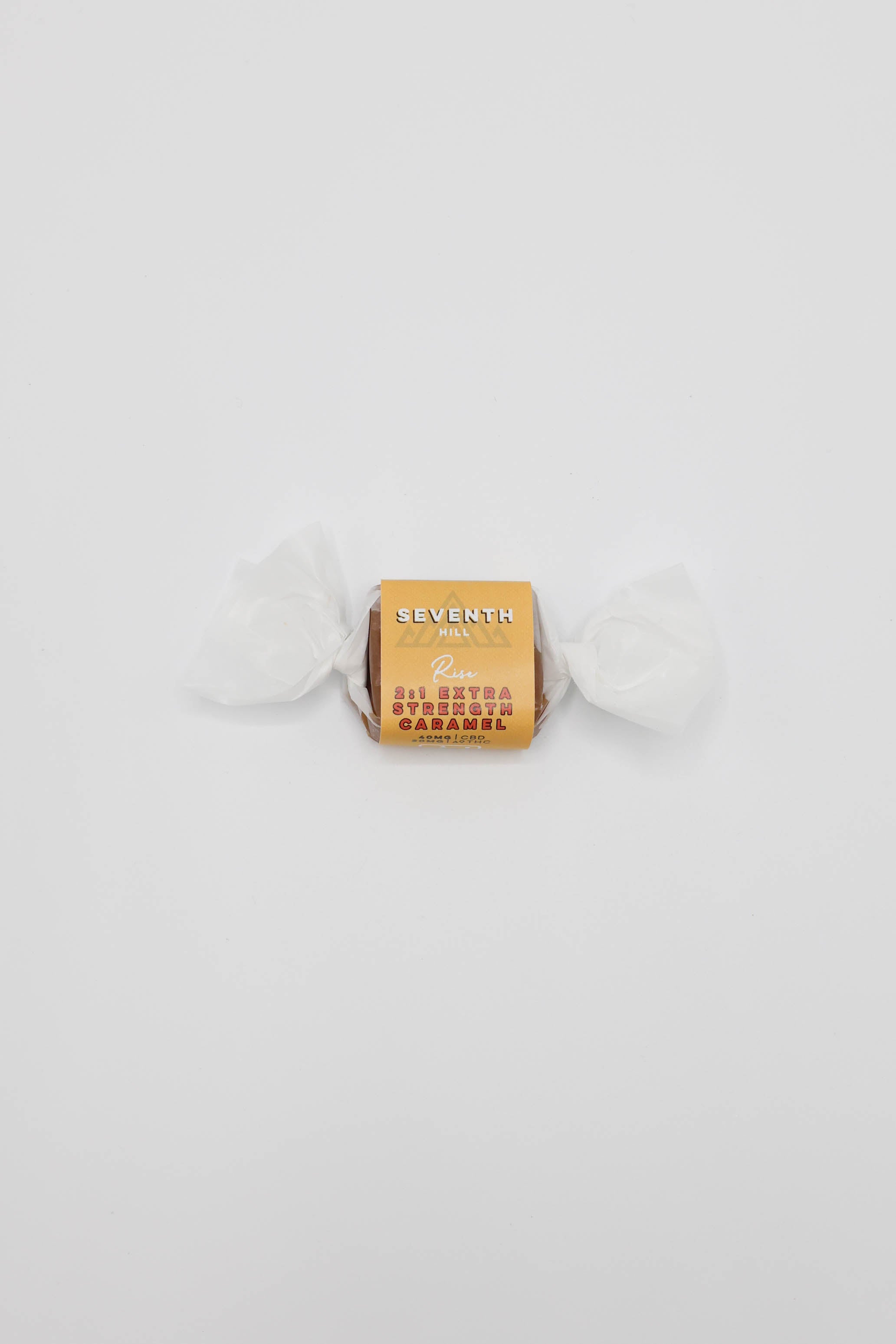 A single wrapped caramel centered on a plain white background. The wrapper is yellow/orange with visible text including 'SEVENTH HILL' and '2:1 Extra Strength Caramel"