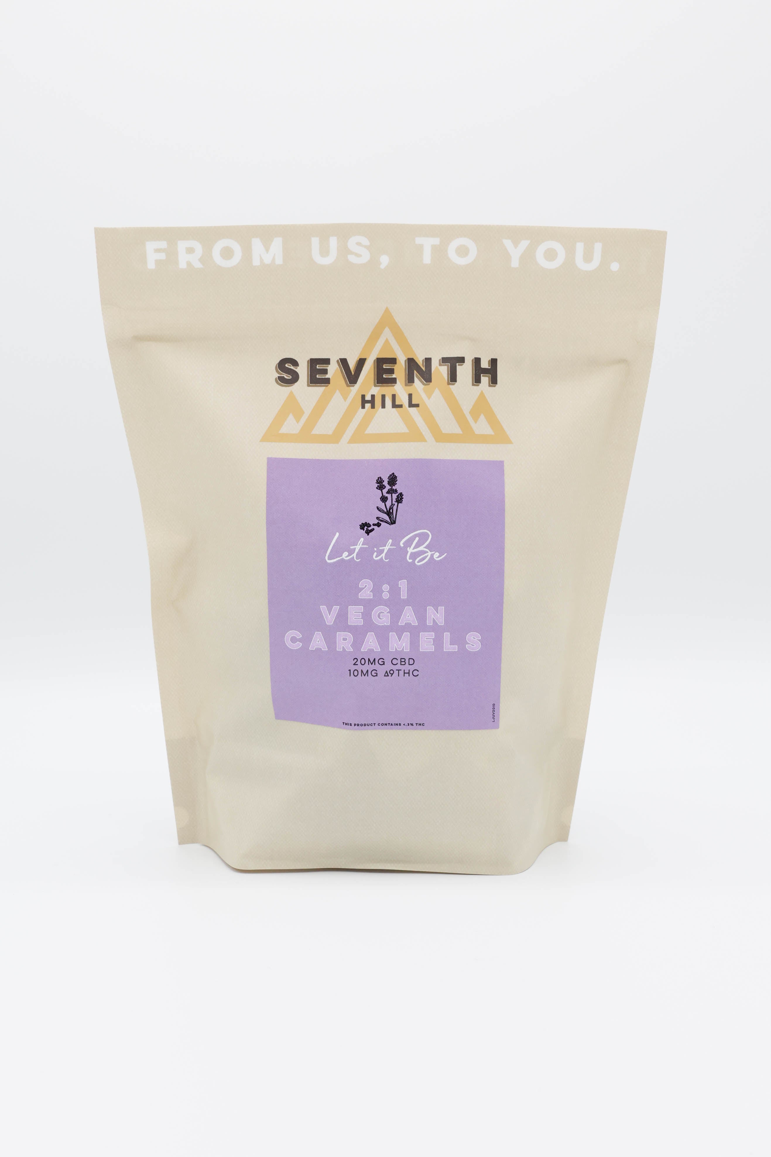 A stand-up pouch of Seventh Hill 2:1 Vegan Caramels on a clean white background. The packaging is a warm cream color with a lavender purple label and gold logo accents.