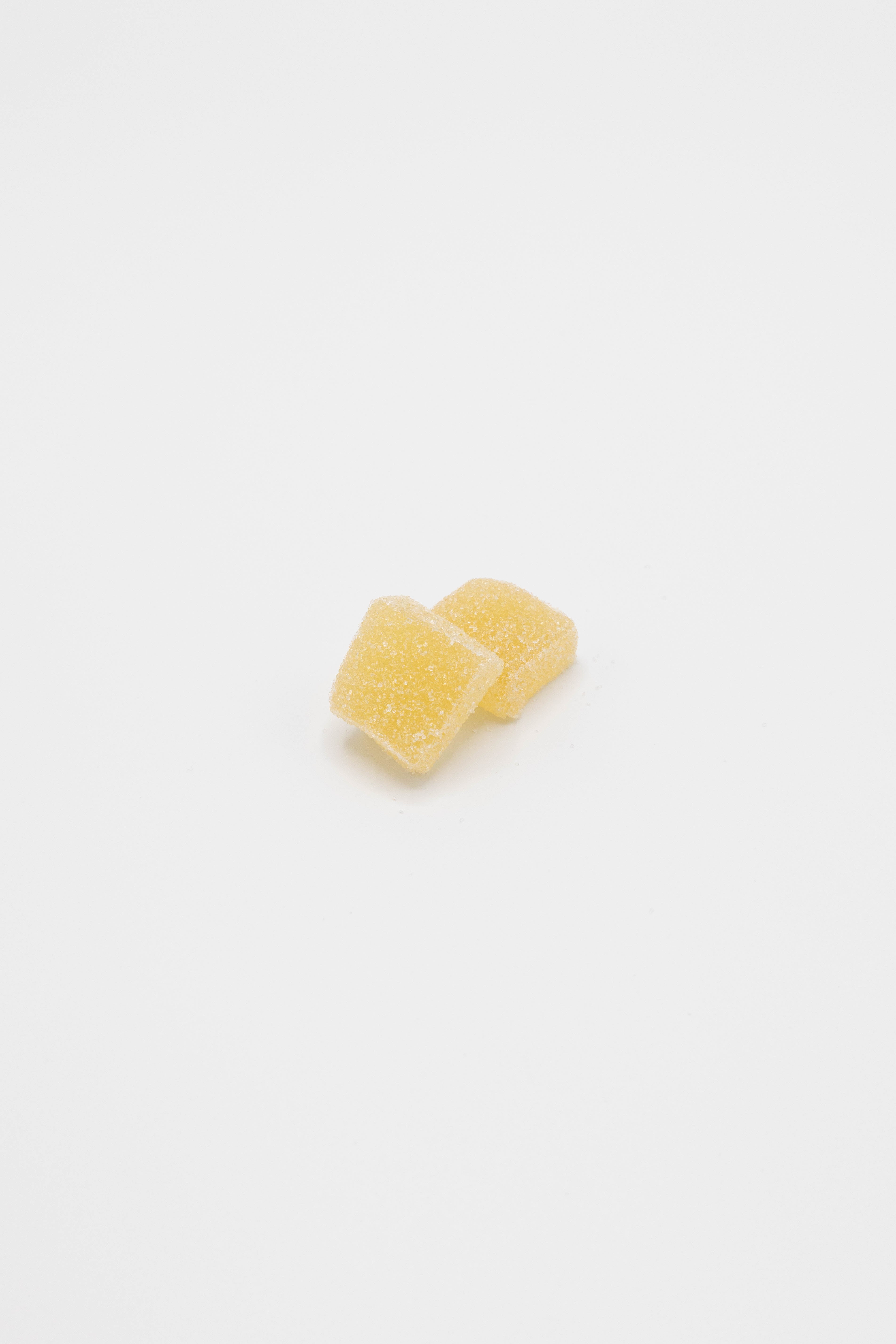 Two small yellow sugar-coated candy cubes on a plain white background.