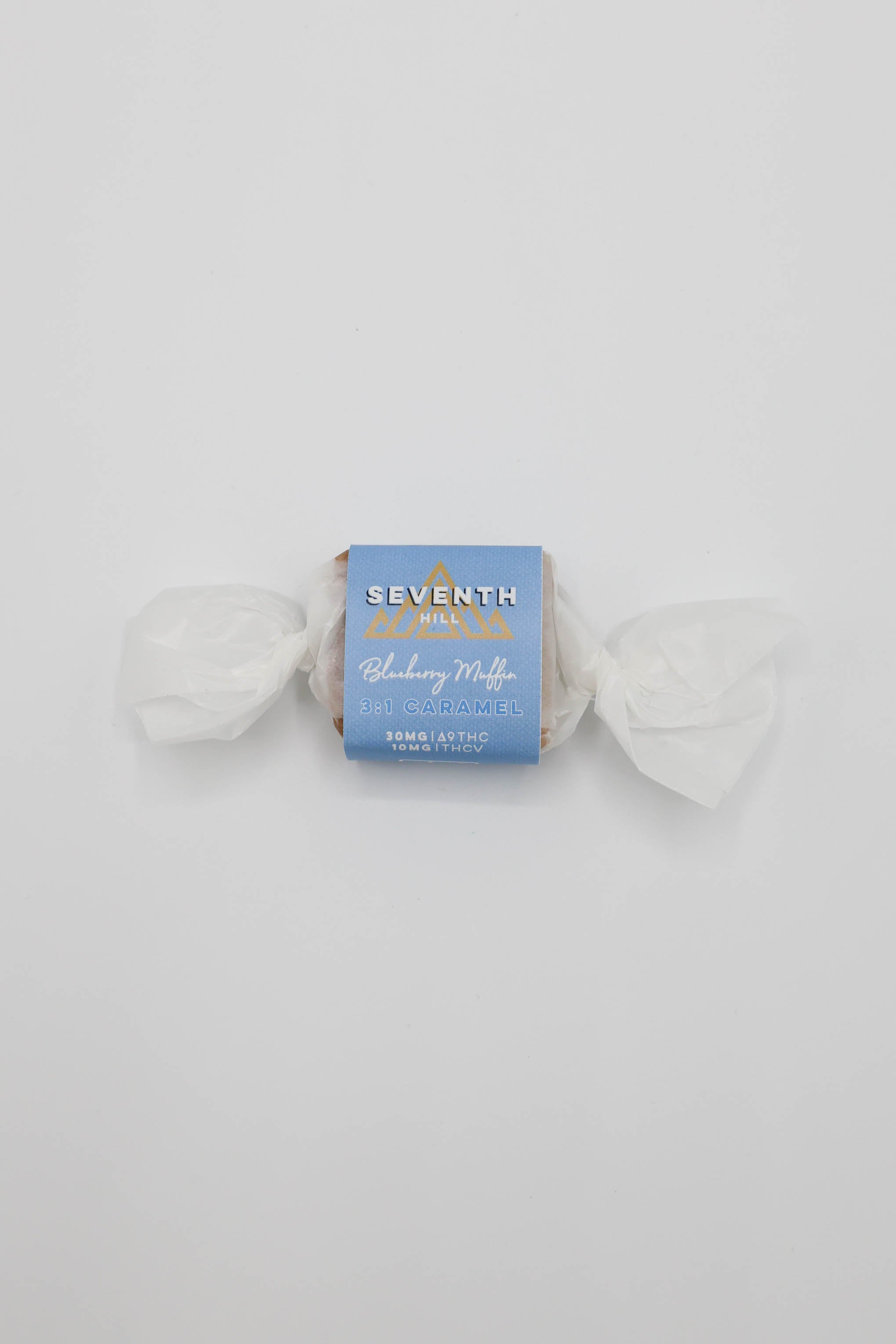 A wrapped piece of caramel from Seventh Hill, featuring a light blue paper label with white text and gold accents, set against a plain white background.