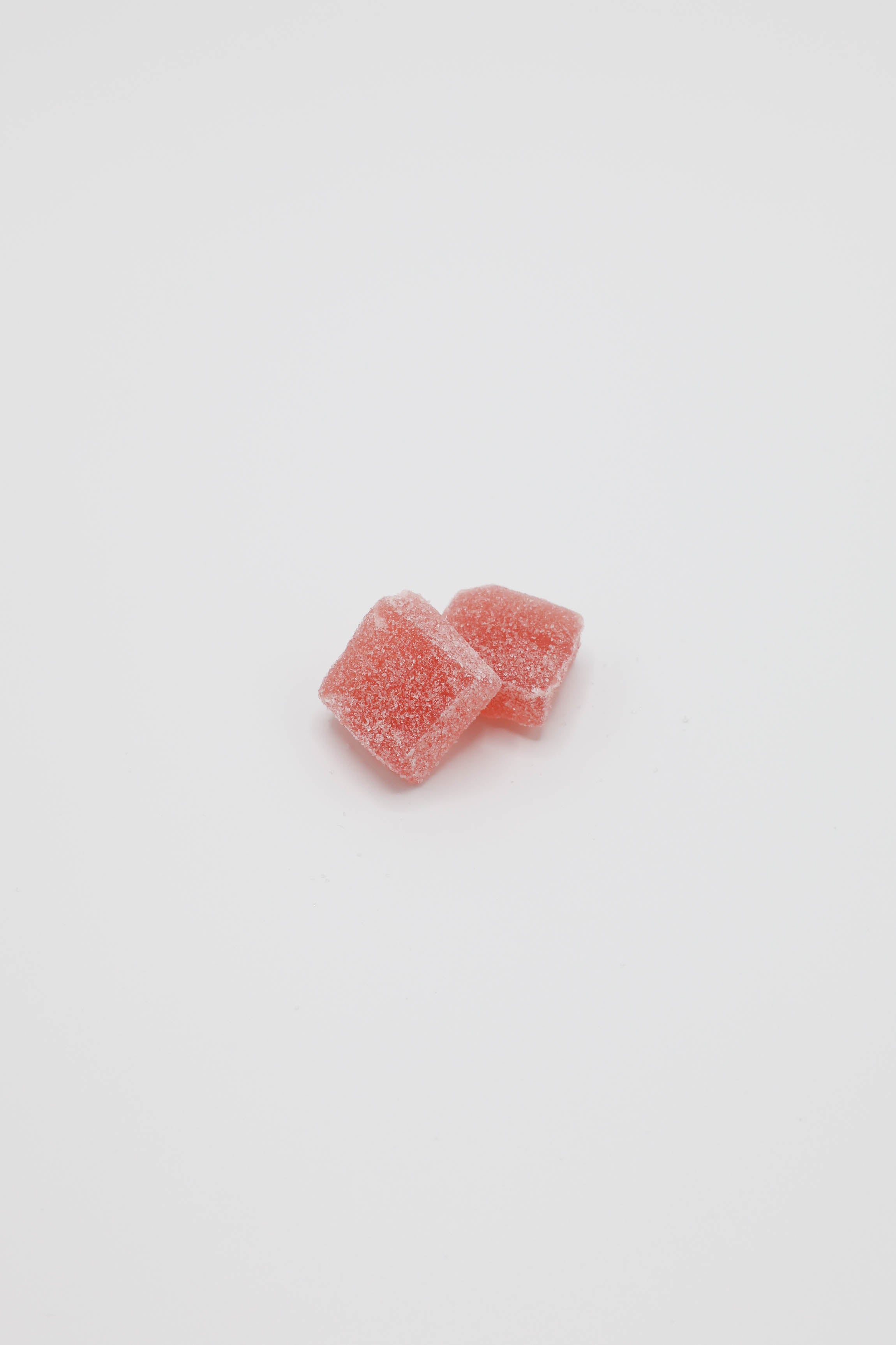 Two small pink sugar-coated candy cubes on a plain white background.