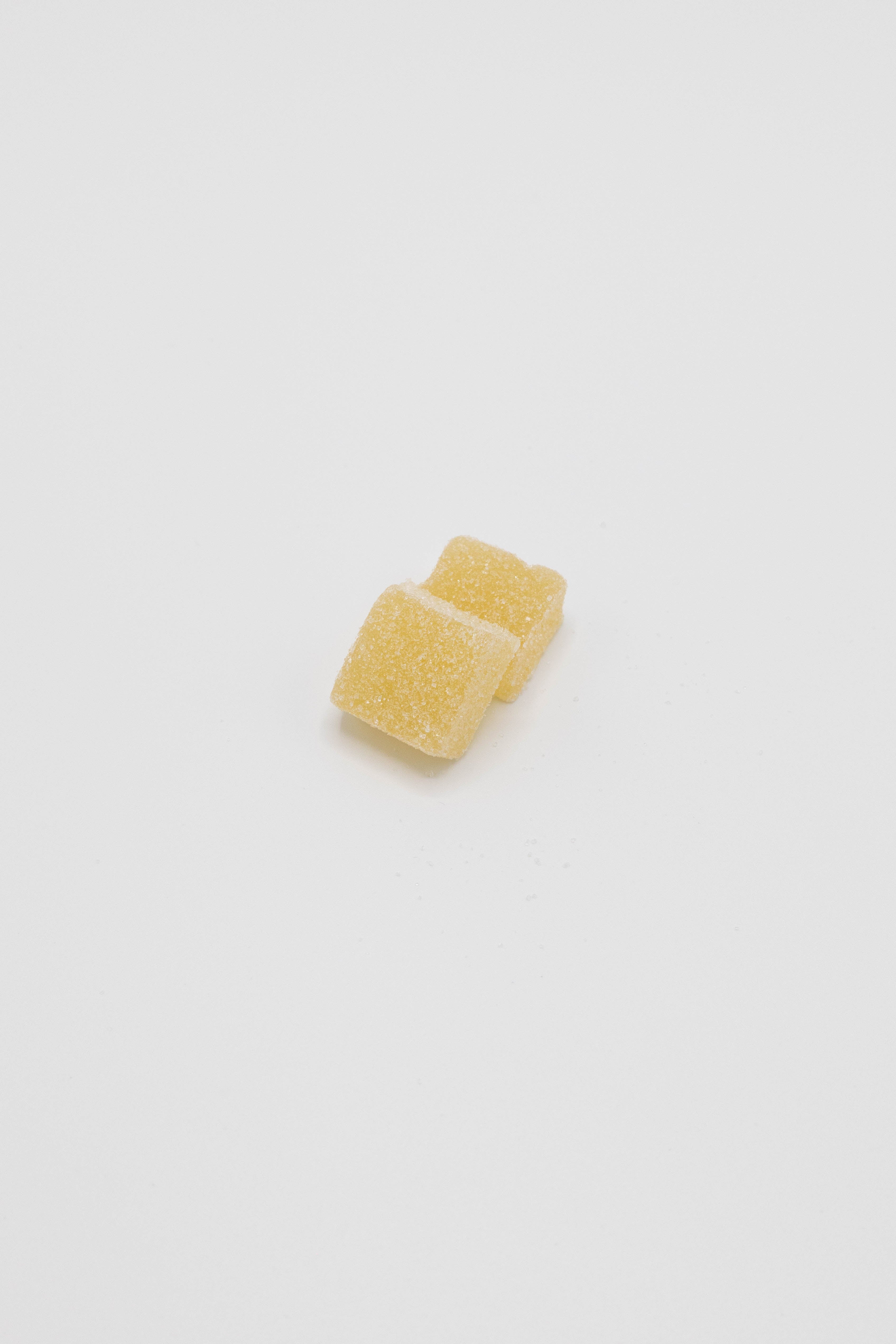 Two small yellow square gummy candies with a sugar-coated texture, photographed on a clean white background.
