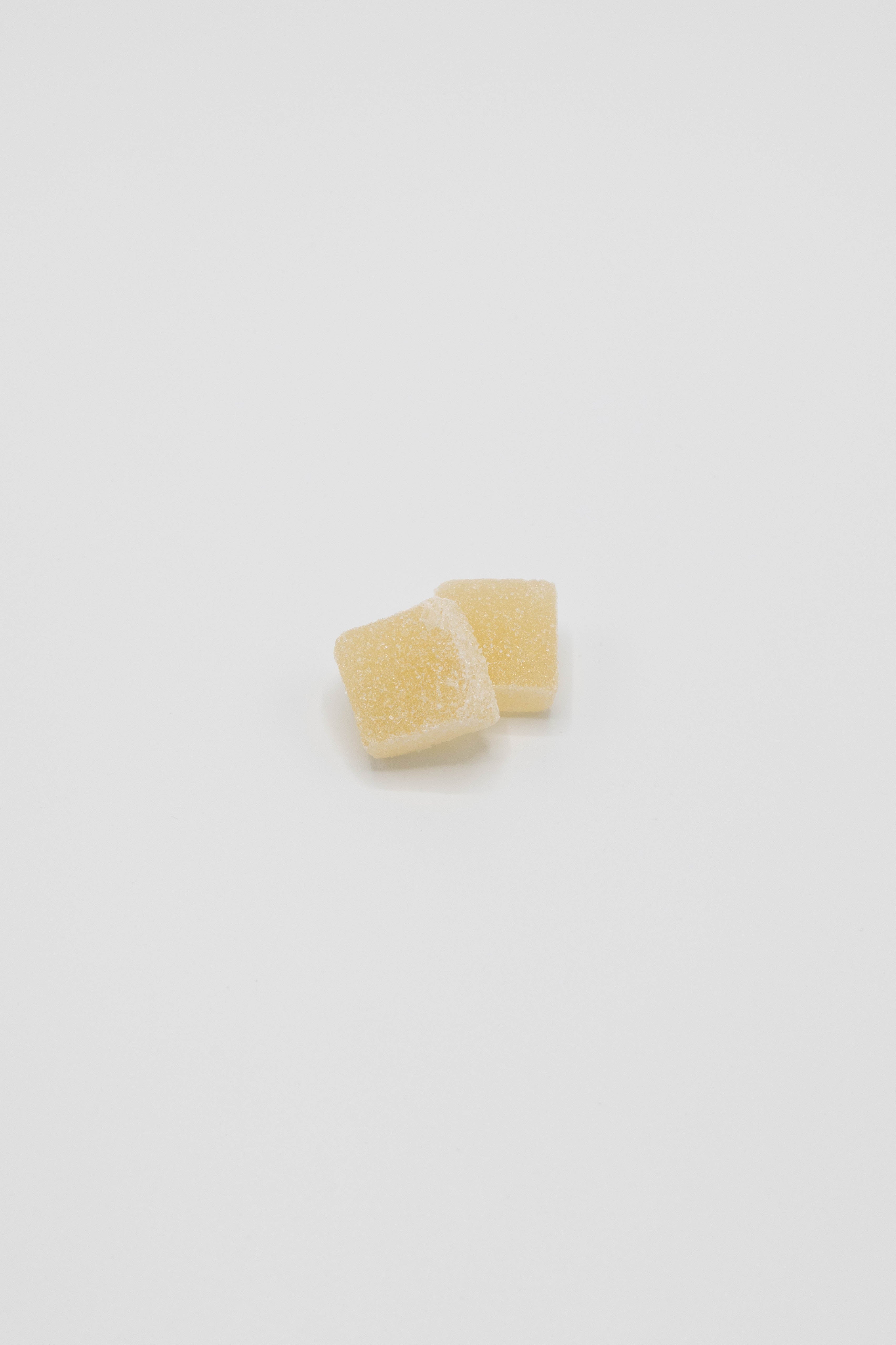 Two small, pale yellow, sugar-coated gummy candies on a seamless white background.