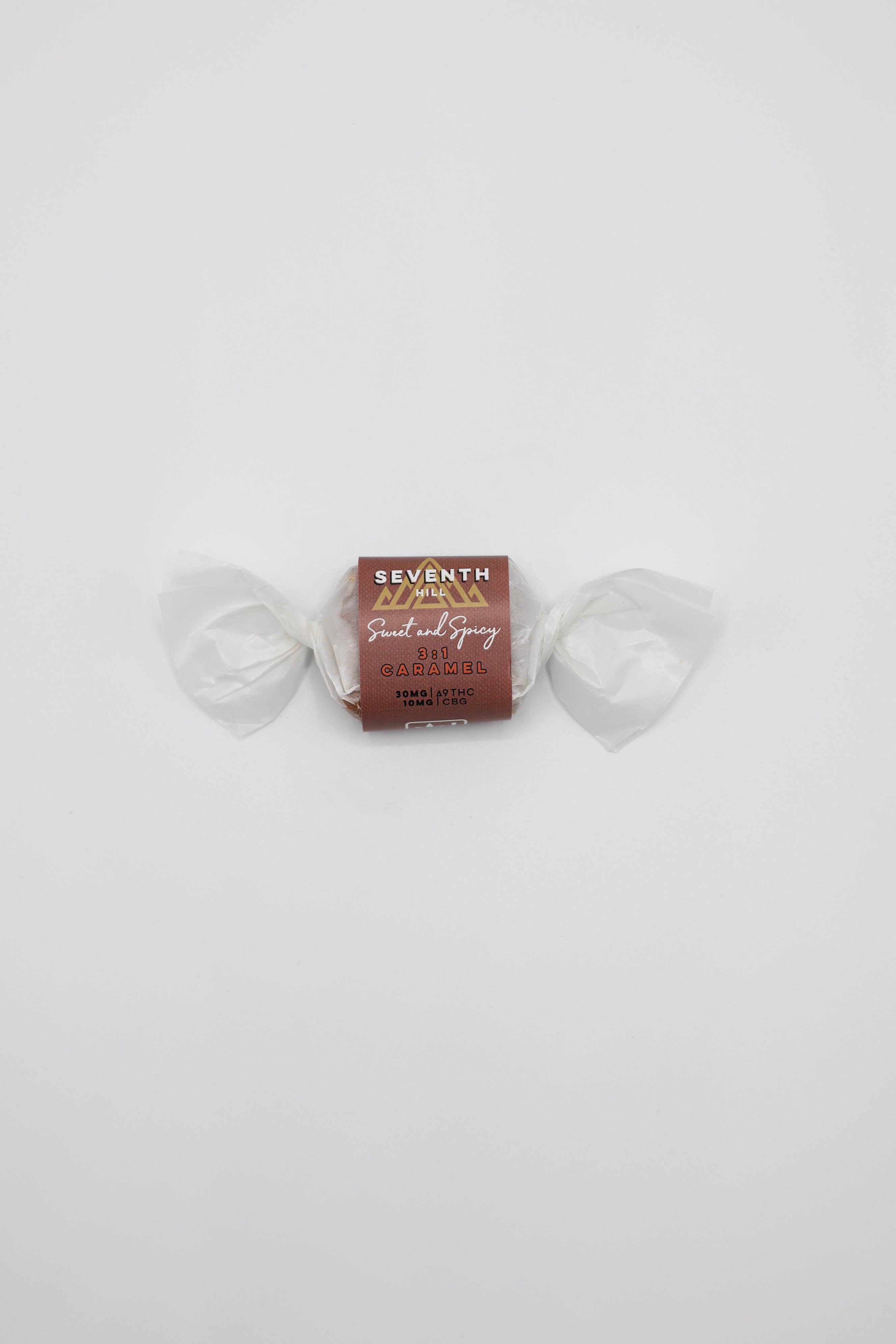 A single wrapped candy from Seventh Hill, featuring a brown/red paper label with gold and white text, on a plain white background.