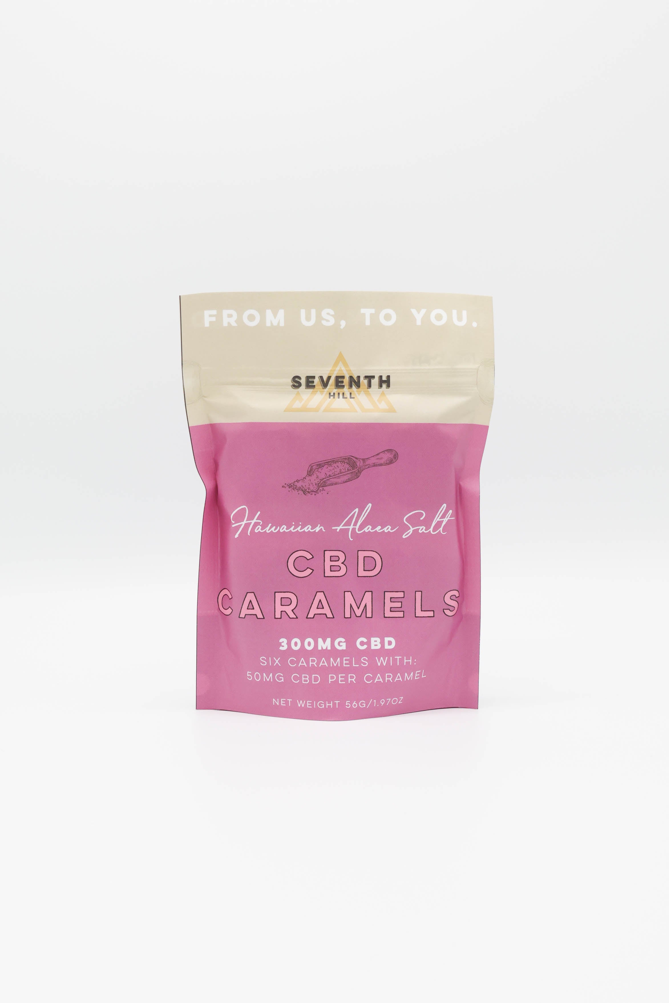 A stand-up pouch of Seventh Hill CBD Caramels on a clean white background. The packaging features a pink lower half with white text reading 'Hawaiian Alaea Salt CBD Caramels 300MG CBD' and a beige top band with 'FROM US, TO YOU.