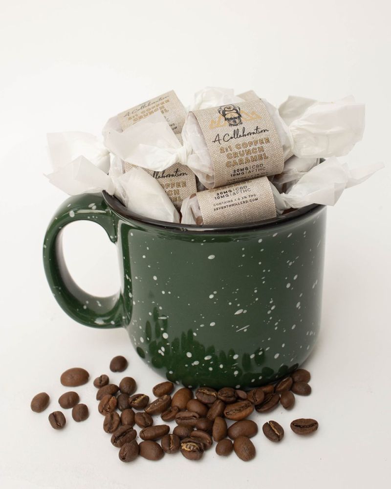 A green coffee mug is filled with 2:1 Coffee Crunch Caramels with coffee beans lying around its base